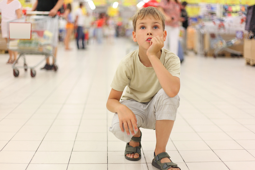 Уставший мальчик сидит на корточках посреди супермаркета