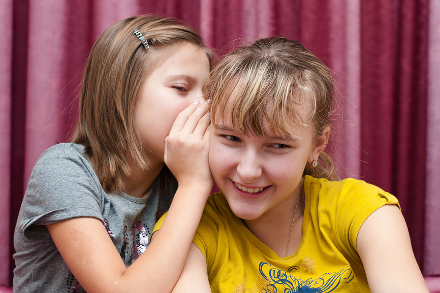 Девочка рассказывает свой секрет подружке на ухо