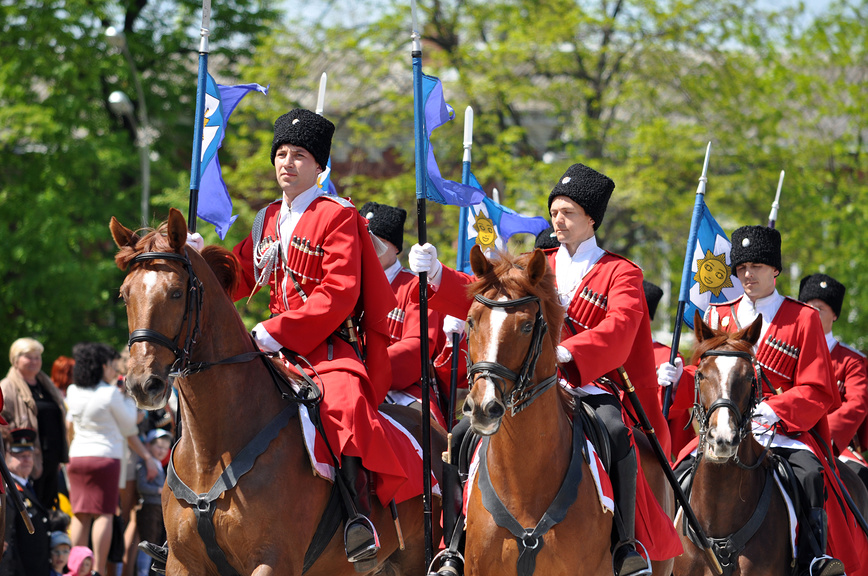 Казаки на лошадях, парадный расчёт, черкески красные, папахи чёрные, знамёна с солнцем, шествие, историческая форма, конный строй, казачья традиция, весенний парад.