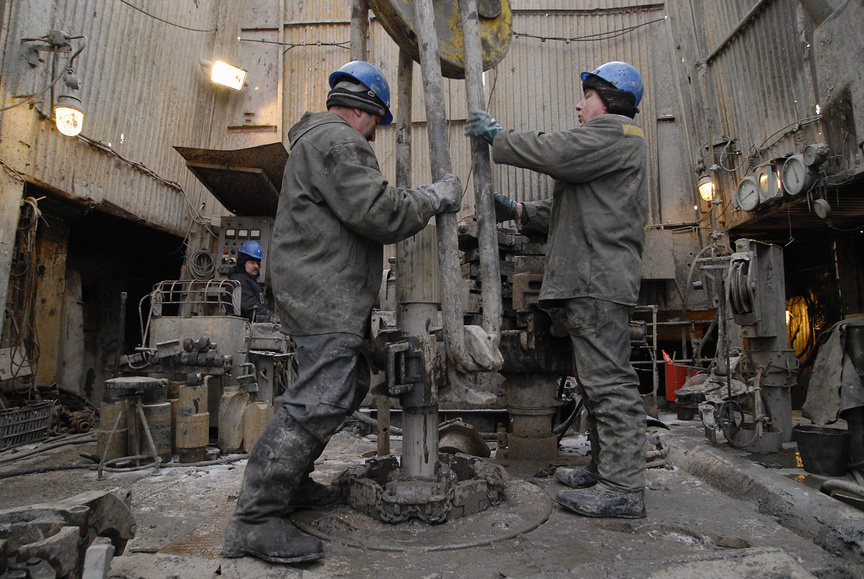 Рабочие-нефтяники закрепляют насос над нефтяной скважиной