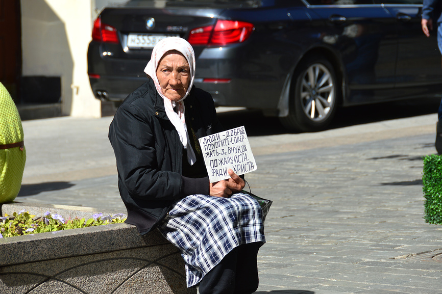 пожилая женщина, сидящая на бордюре у дороги.