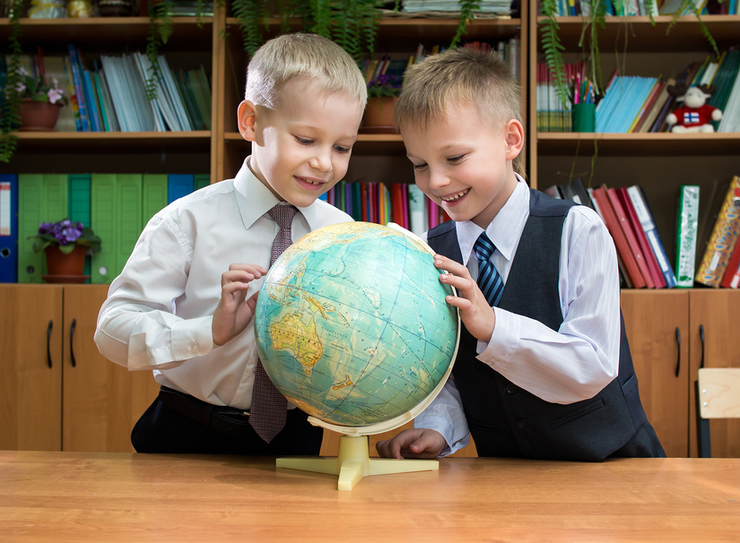 Два мальчика в школьной форме с интересом рассматривают глобус, стоящий на столе