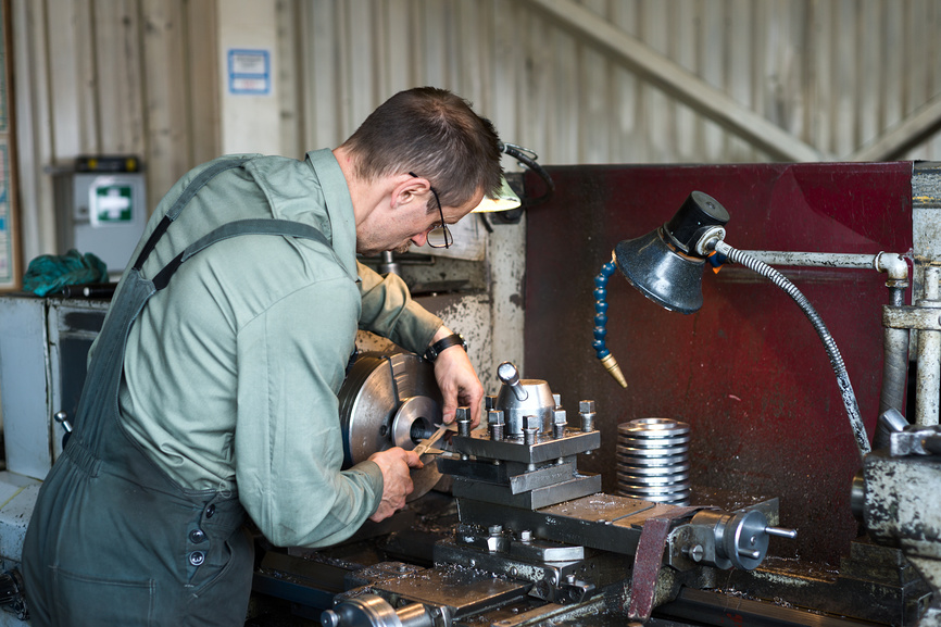 Токарь работает на токарно-механическом станке. Токарные работы, обработка металла резанием.