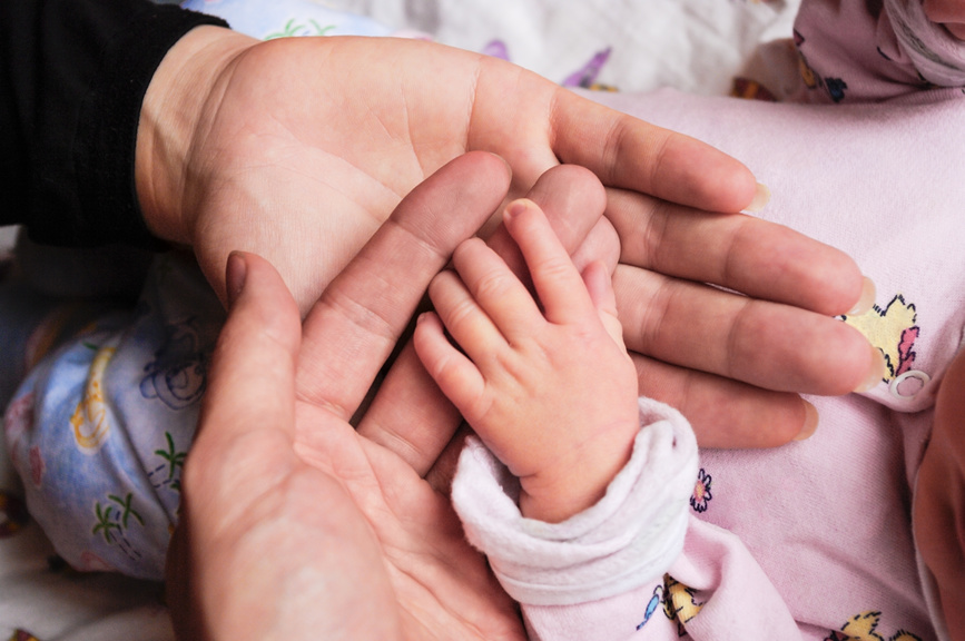 руки взрослого и ребёнка: маленькая детская ладошка аккуратно лежит в ладонях взрослого.