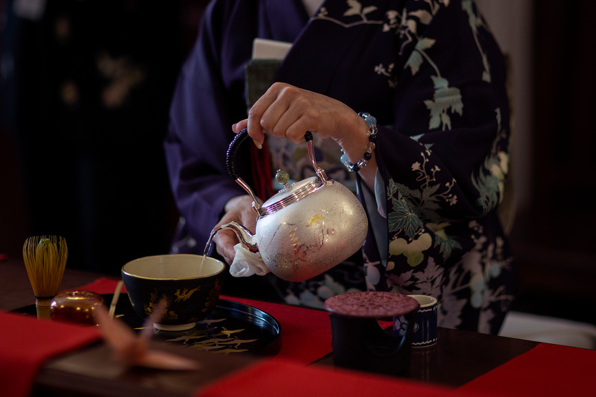 Женщина в кимоно наливает горячую воду из чайника в чашку с чаем во время традиционной японской чайной церемонии