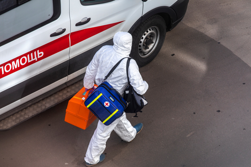 сотрудник скорой помощи в белом защитном костюме, выходящий из машины с надписью