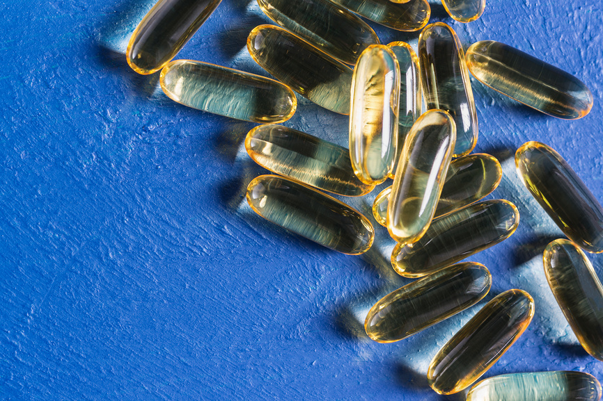 Прозрачные желатиновые капсулы с рыбьим жиром лежат на фактурной синей поверхности.