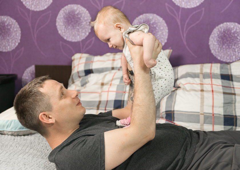 Папа играет с младенцем дома на кровати