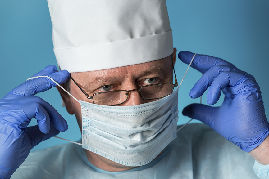 Врач в очках и перчатках надевает медицинскую маску