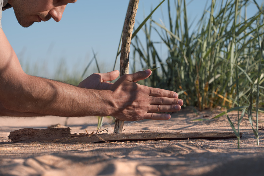 Мужчина пытается разжечь огонь без спичек и зажигалки. Выживание в диких условиях