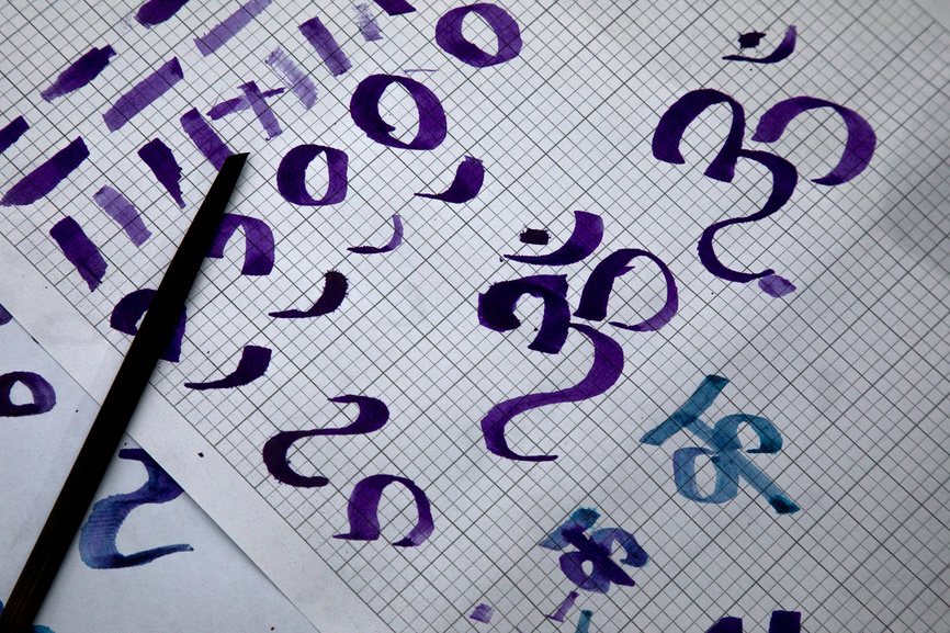 Листок бумаги с написанными буквами древнего восточного языка санскрита и специальная палочка для написания чернилами