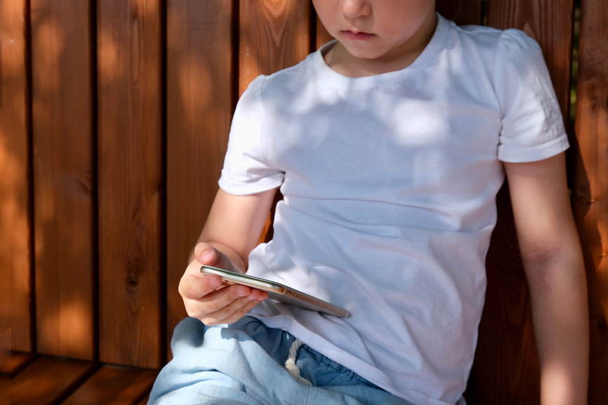 Ребенок пользуется смартфоном на улице.
