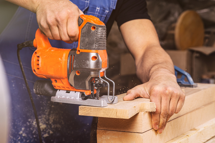 Крупный план опытного плотника в рабочей одежде и плотника-владельца малого бизнеса, который распилил и обработал края деревянного бруска лобзиком в мастерской.