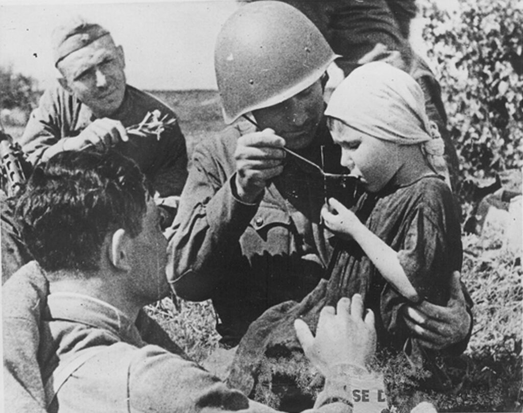 советский солдат в каске кормит маленькой ложкой девочку